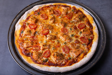 Pizza with salmon, tomatoes and capers. Whole pizza on a black background. Close-up.