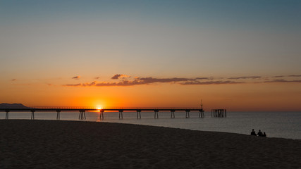 Obraz premium group of friends sitting on the beach watching the sunrise