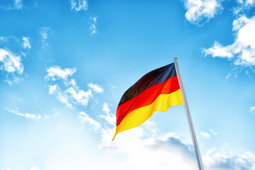 A German flag in front of clouds in blue sky