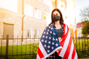Girl in protective black medical mask wrapped in american flag . Pandemic in quarantine city. Preventing the spread of the epidemic of coronavirus.