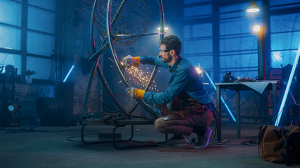 Handsome Male Artist Uses an Angle Grinder to Make Brutal Metal Sculpture in Studio. Hipster Guy. Contemporary Fabricator Creating Abstract Steel Art.