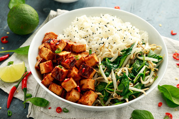 Fried tofu in sweet chilli glaze served with rice, steamed spinach and beansprouts in white bowl. Vegetable healthy food