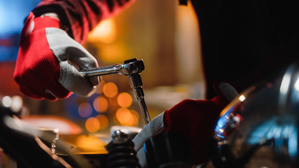 Close Up Footage of a Mechanic Bike Enthusiast in Red Work Gloves in a Garage or a Creative Workshop. Talented Person Working on a Custom Bike with a Ratchet.