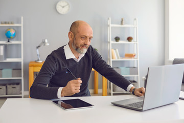 An elderly man works using a laptop office at home.