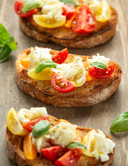 Tomato bruschetta and mozzarella cheese with basil on a rustic wooden board