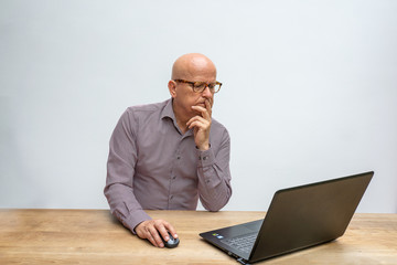 caucasian male middle aged and with glasses, sitting behind a desk working with his lap top