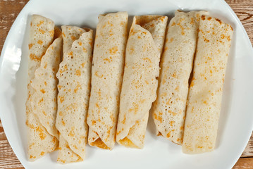 Pancakes are twisted into a tube and stuffed with cheese. Food in a white plate on a wooden table. Pancakes on a background of pink boards.