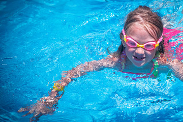 Portrait of little cute young girl in water glasses practice swimming in the outdoor pool. The child in the outdoor pool at the resort.