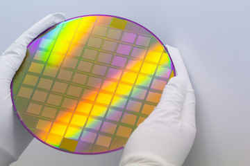 Hands in white gloves holding a silicon wafer with microchips on white background.Banner format.