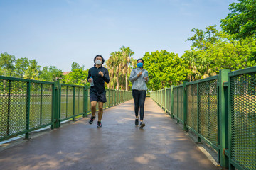 Asian couples wear masks that protect against covid 19 so happy and jogging together for health in the park.Social distancing and New normal concept.