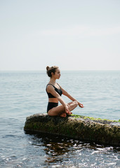 Fototapeta na wymiar Woman practicing yoga sitting in lotus pose at seaside 