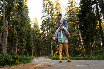 a young couple walks through the woods, a girl sits on a guy’s shoulders, a guy with a girl is surprised at what is happening