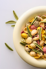 uncooked colored homemade pasta in a bowl close-up on a white table, top view