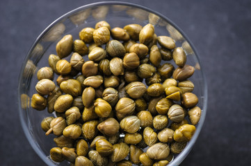 pickled capers in a glass bowl on a dark background, top view close up