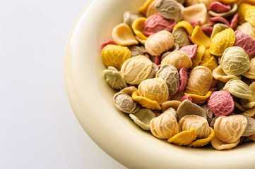 uncooked colored homemade pasta in a bowl close-up on a white table, top view