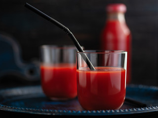 tasty tomato juice poured into glasses with a cocktail straw, a bottle of juice in the background, dark background