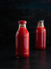 two bottles with tomato juice on a dark background