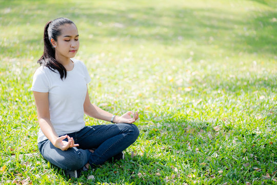 Asian young women meditation yoga with smile face for peace, relaxation emotional on green grass of park with natural light sunset of the sun with dramatic yellow and orange sky. Image depth of field.