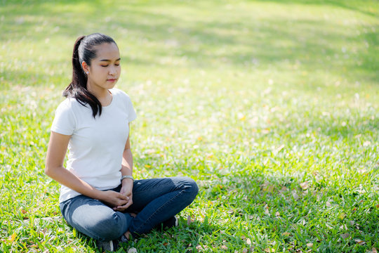 Asian young women meditation yoga with smile face for peace, relaxation emotional on green grass of park with natural light sunset of the sun with dramatic yellow and orange sky. Image depth of field.