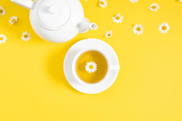Obraz na płótnie Canvas White chamomiles, cup and teapot on yellow background. Herbal tea of chamomile flower. Chamomile tea concept. Flat lay, top view, copy sp