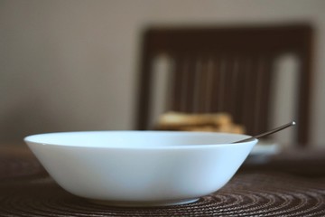 breakfast, holy plate with a spoon on the table. unusual angle. wooden chair