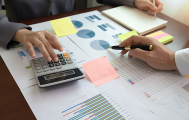Businessman analysis on graph data report paper with businesswoman using calculator and writing make note on the table at the business office.The concept of working together for success.