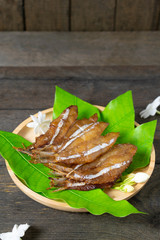 Fried dried fish on mango leaf in wooden dish on wooden table.