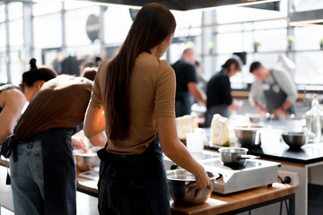 Culinary class. Back view of the process of cooking. Different unrecognizable people in gray apronsthe in the kitchen learn to cook