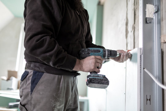 Ein Handwerker befestigt eine Gipsplatte mit einer Bohrmaschine an der Wand