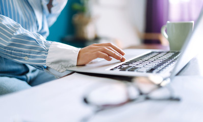 Close up picture of females hands on the keyboard. Young woman working with laptop sitting in modern living room at home. Technology, freelance and work concept.