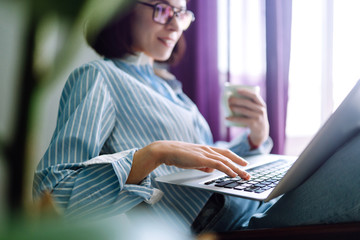 Close up picture of females hands on the keyboard. Young woman working with laptop sitting in modern living room at home. Technology, freelance and work concept.