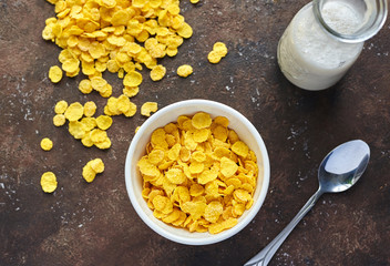 yellow cornflakes with milk in a white deep plate on a brown table