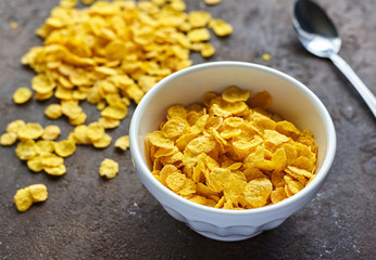 yellow dry corn flakes in a white deep plate on a brown table