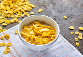 yellow cornflakes with milk in a white deep plate on a brown table