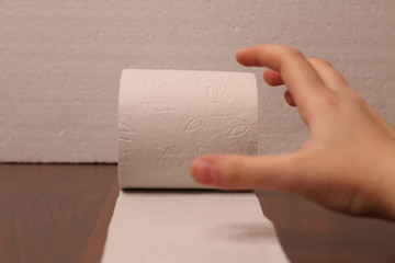 The hand reaches for a roll of white toilet paper