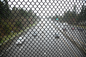 Fototapeta premium Chainlink fence on a freeway overpass, with traffic in the blurry background