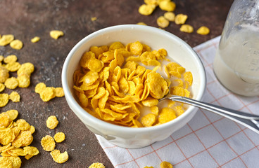 yellow cornflakes with milk in a white deep plate on a brown table