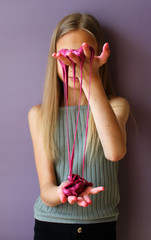A blonde preteen girl playing with handmade pink slime on violet background. The focus is on slime. Activities and educational games with children at home. Hobby DIY