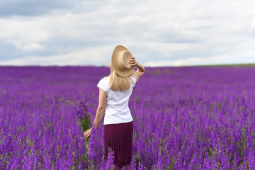 A girl in a straw hat with a bouquet of wildflowers in a lushly blooming lavender field with flowers.