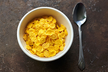 yellow dry corn flakes in a white deep plate on a brown table