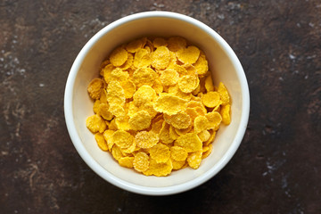 yellow dry corn flakes in a white deep plate on a brown table
