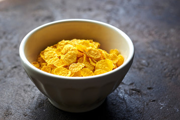 yellow dry corn flakes in a white deep plate on a brown table