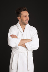 Happy young man in bathrobe on black background