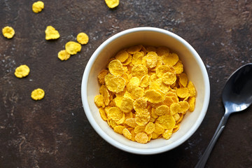 yellow dry corn flakes in a white deep plate on a brown table