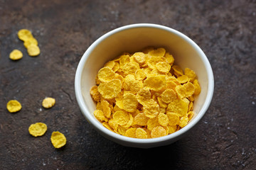 yellow dry corn flakes in a white deep plate on a brown table