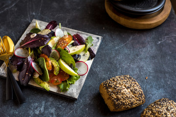 delicious tomato and guacamole lettuce salad, with green apple and radish on dark background