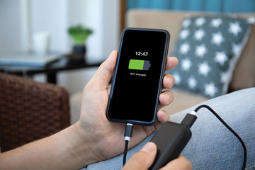Man hands holds phone charged battery and power bank charge