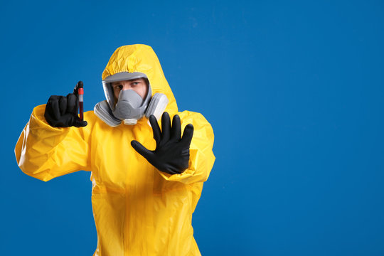 Man in chemical protective suit holding test tube of blood sample on blue background, space for text. Virus research
