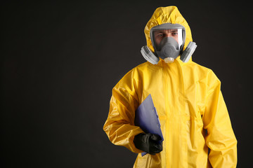 Man in chemical protective suit holding clipboard on black background, space for text. Virus...