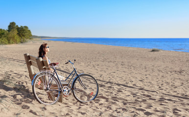 Fototapeta premium Middle-aged woman came on a Bicycle to the beach and resting sitting on a bench.